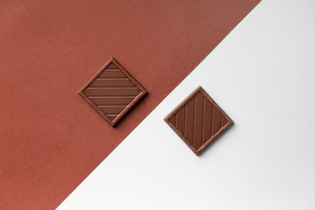 Two chocolate bars on colored backgrounds top view. Small chocolate bars on white and brown backgrounds. Conceptual composition of two chocolate bars on contrasting backgrounds.の写真素材
