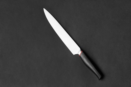 Kitchen knife with a black handle on a black background. Large knife on a dark background top view....