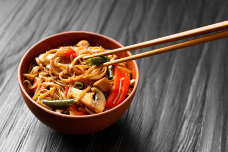 Plate with buckwheat noodles with vegetables, mushrooms, chicken meat and Chinese sticks on a dark...