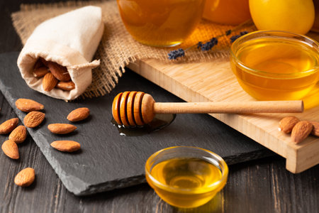 Honey in jars and a bowl, dipper, lemon, ginger, almond on a black stone plate on a wooden background. Conceptual composition of useful organic products. Natural products for the treatment of colds.の写真素材