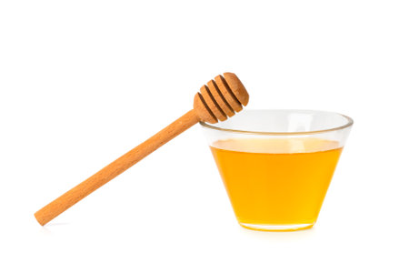 Fresh honey in a glass transparent bowl with a wooden dipper on a white isolated background. Honey in an open glass jar with a honey stick. Honey on a white background.の写真素材
