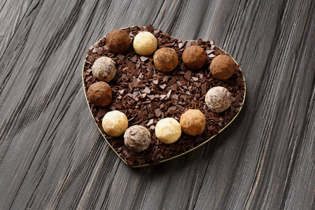 White, milk and dark chocolate truffles and chocolate chips in a heart-shaped box on a dark wooden...