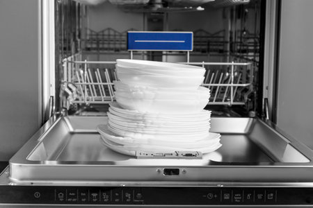 Built-in dishwasher with open door and clean dishes. Clean white plates sit on the open door of the dishwasher. Household appliances for the kitchen.の写真素材