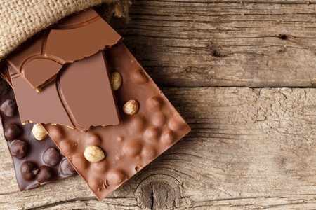 Handmade dark and milk chocolate with hazelnuts in a burlap bag on an aged wooden background, top view. Handmade chocolate concept.の写真素材
