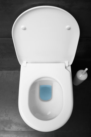 Top view of a white toilet bowl with a raised lid against a black ceramic floor.の写真素材