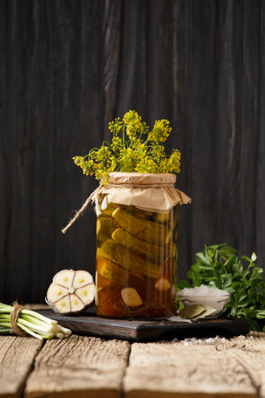 Homemade canned cucumbers in a jar, garlic, spices and herbs for marinade on a wooden background.の写真素材