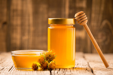 Creative composition of honey in a glass jar and a bowl, a wooden dipper and yellow flowers on an aged wooden background. The concept of organic bee products.の写真素材