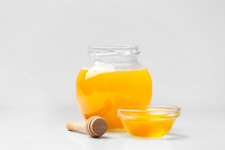Organic honey in a glass jar and a transparent bowl, wooden dipper on a white background. Spoon for honey and fresh honey in an open jars on isolation close-up. health products.の写真素材