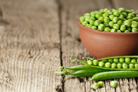 Peeled green peas in a clay bowl, sweet organic green peas in closed and open pods and scattered grains on an aged wooden background, copy space. vegetable proteins.の写真素材