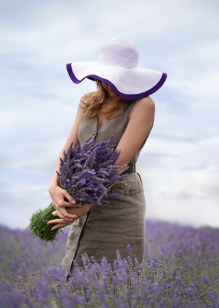 Girl in a dress and hat with a bouquet of lavender in her hands in a field of blooming lavenderの写真素材