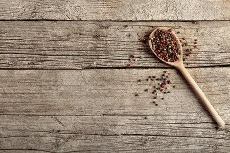 Mix of peppers with peas in a wooden spoon on a wooden background, top view. Red pepper, white pepper and green pepper.の写真素材