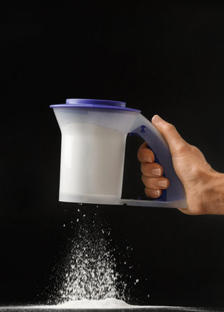 A woman's hand holds an eco-plastic sieve on a black background and sifts the flour. kitchenware.