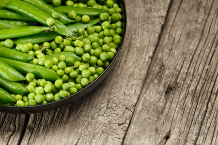 Green pea pods and shelled organic fresh peas in a round black plate on an aged wooden background, copy space. Vegetable protein, healthy products.の写真素材
