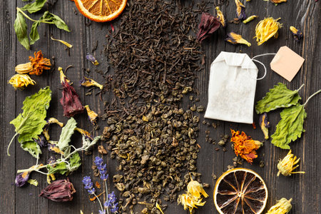 Composition of dry black and green tea, tea bag, dried citrus slices and dry hibiscus flowers on a dark wooden background top view. Different types of dry tea on a dark background.の写真素材