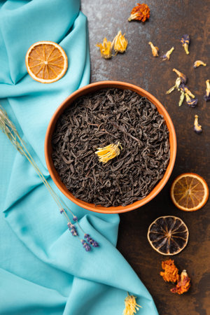 Composition of dry black tea leaves in a bowl, flower tea and dry orange slices on blue and brown backgrounds top view. Large-leaf tea and citrus chips on contrasting backgrounds.の写真素材