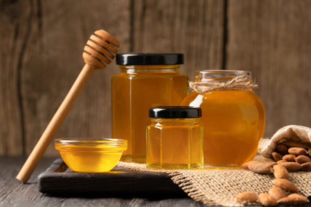 Creative composition of honey in a glass jar and a bowl, a wooden dipper and yellow flowers on an...