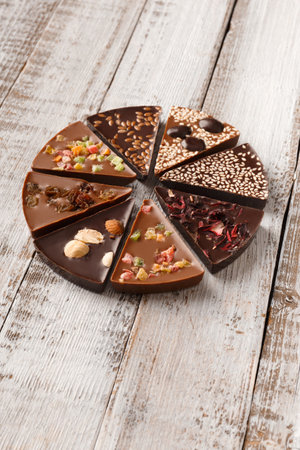 Creative composition chocolate in the shape of a pizza with candied fruits, nuts, dry berries, chocolate pizza and ingredients on a wooden background.の写真素材