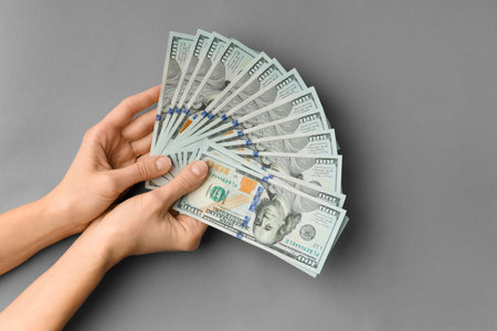 A lot of bills of 100 dollars in hands are folded in a fan on a gray background top view with space...