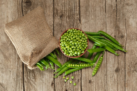 Pods of fresh green peas in a burlap bag, shelled peas in a clay bowl, sweet organic green peas in closed and open pods on an aged wooden background, top view. vegetable proteinの写真素材