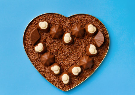 Heart-shaped box with chocolates and chocolate chips on a blue background, top view. Postcard, template for Valentine's Day.の写真素材