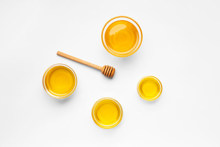 Creative composition of honey in glass bowls of different sizes and a wooden dipper on a white background top view. Organic honey and honey spoon on isolation.の写真素材