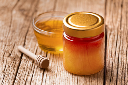 Organic honey in a closed glass jar and in a transparent glass bowl, wooden dipper on a rustic wooden background, close-up.の写真素材