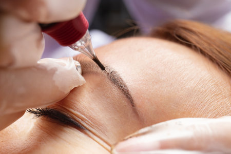 Beauty master performs permanent eyebrow makeup in a beauty salon, close-up. Hands of a cosmetologist doing microblading of eyebrows. Tattoo on the face.の写真素材