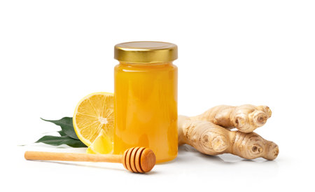 Organic honey in a closed glass transparent jar, a wooden dipper, ginger and a cut lemon with green leaves isolated on a white background. Honey, honey stick and citrus fruits close-up.の写真素材