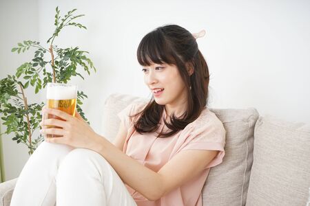 Young woman drinking beer at homeの写真素材