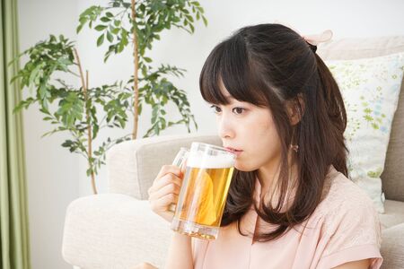 Young woman drinking beer at homeの写真素材