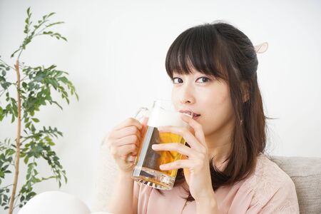 Young woman drinking beer at homeの写真素材