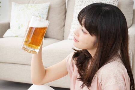 Young woman drinking beer at homeの写真素材
