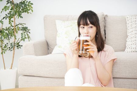 Young woman drinking beer at homeの写真素材