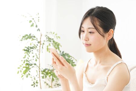 Young woman using a smart phone in her roomの写真素材