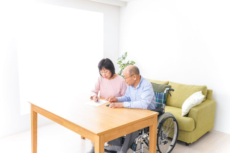 Senior man in wheelchair and woman in wheelchair doing paperwork at home.の写真素材