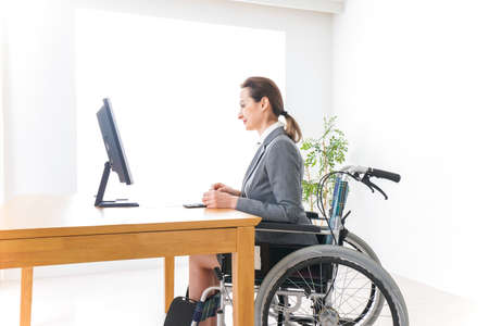 Disabled businesswoman in wheelchair working at the computer in the officeの写真素材