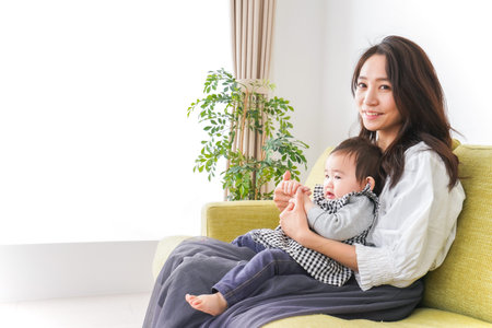 Young woman and baby sitting on sofa in living room. Happy family concept.