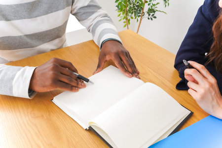 Close-up Of A Couple Writing In Notebook At Desk