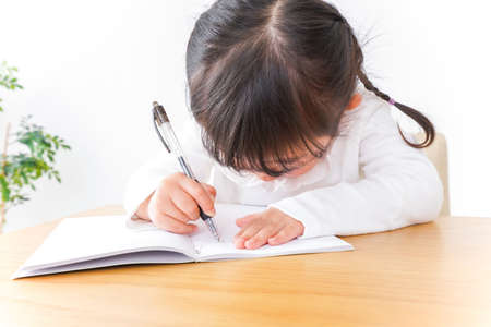 Child writing in a notebook at the desk, shallow depth of fieldの写真素材