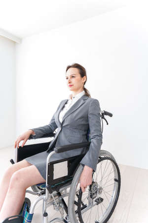 Businesswoman sitting in a wheelchair in an office building.の写真素材
