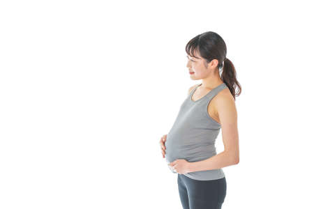 Pregnant woman in sportswear standing against white background.の写真素材