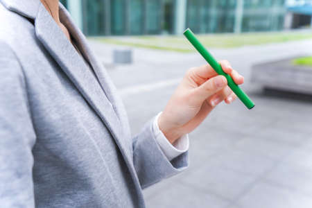 Businesswoman holding a green pen on the background of an office buildingの写真素材