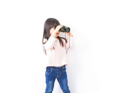 Young girl watching through binoculars shot in the studio on a white backgroundの写真素材