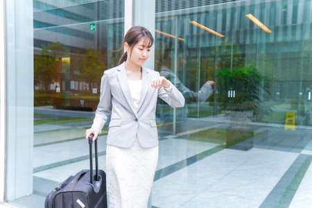Businesswoman with luggage at the entrance of the office (shallow DOF; color toned image)の写真素材