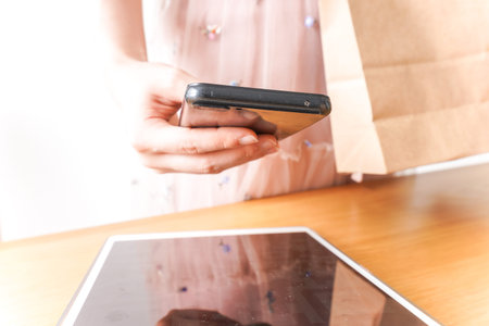Woman using smart phone with shopping bag and digital tablet on wooden table
