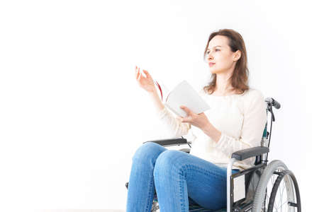 Young woman in a wheelchair reading a book - isolated on the white backgroundの写真素材