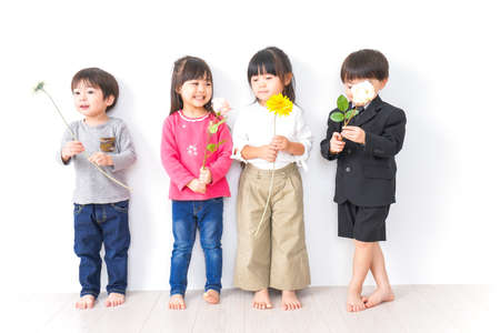 Group of children with flowers in front of a white wall shot in the studioの写真素材