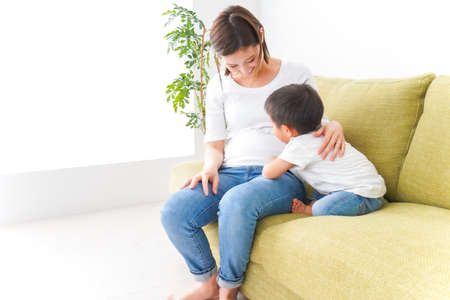 Pregnant woman and her son sitting on the sofa at homeの写真素材
