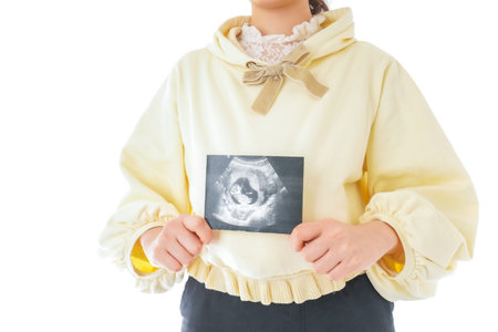Pregnant woman holding ultrasound scan on white background, closeup