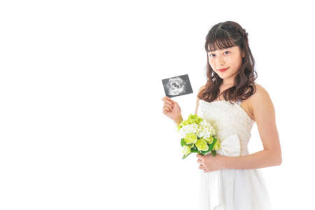 A young bride wearing a wedding dress holding an ultrasound image taken in the studioの写真素材
